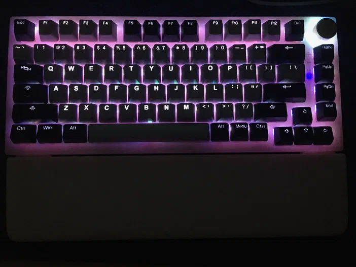 Un clavier mécanique à touches noires dont les switchs émettent une lueur rose.