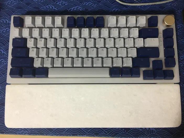 Un clavier mécanique Feker IK75 Pro aux touches grises et bleues posé sur un tapis bleu à motifs.