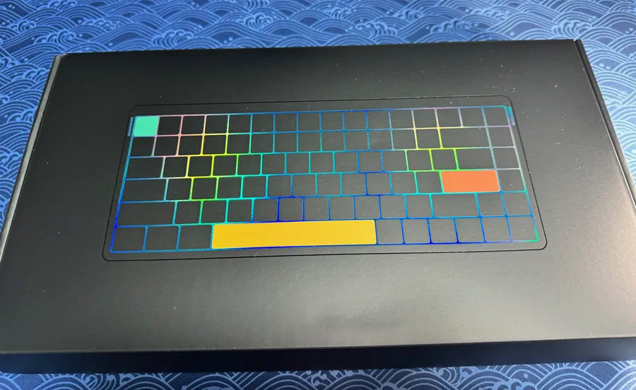 Extérieur du packaging du clavier. On notera que les couleurs changent avec l'orientation pour un rendu réel beaucoup plus sobre et classieux