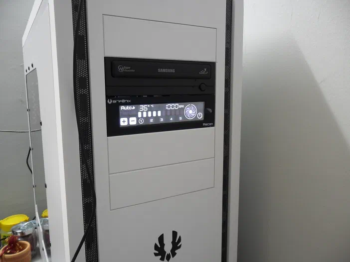 Boîtier informatique blanc contenant un lecteur optique Samsung et le contrôleur de ventilateur Bitfenix Recon avec son écran numérique allumé.