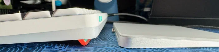 Vue de profil d'un clavier Nuphy Air75 blanc à gauche et d'un Magic Trackpad Apple argenté à droite sur une surface bleue.