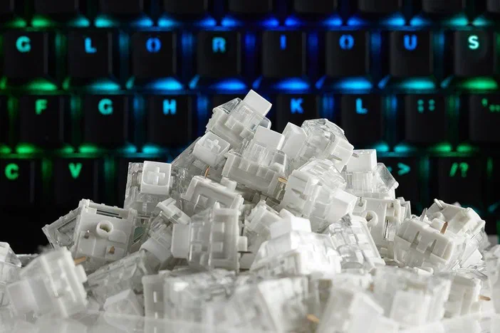Un tas de switches mécaniques blancs empilés devant un clavier rétroéclairé aux couleurs arc-en-ciel.