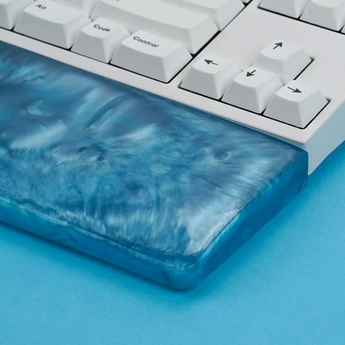 Un repose-poignet en résine bleue marbrée fixé à un clavier blanc avec des touches personnalisées.