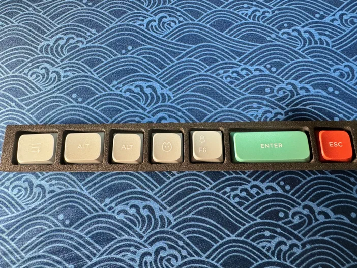Une rangée de keycaps Nuphy Air75 v2 avec des touches ALT, ENTER et ESC sur fond bleu motif vague