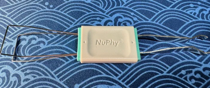 Un keycap-puller NuPhy avec des pinces métalliques sur un fond bleu à motifs.
