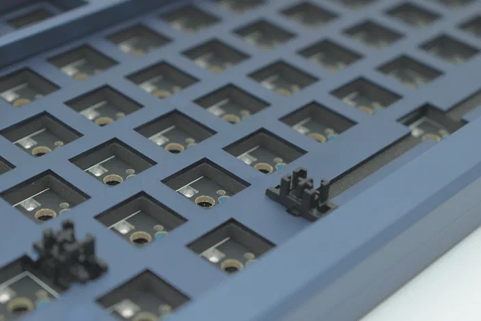 Vue rapprochée d'un clavier mécanique bleu avec des interrupteurs noirs visibles dans les alvéoles.