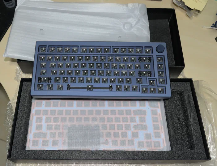 Un clavier mécanique bleu posé sur sa mousse de protection dans un boîtier noir.