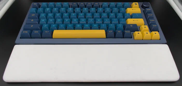 Clavier mécanique avec des touches bleues et jaunes sur un repose-poignets blanc.
