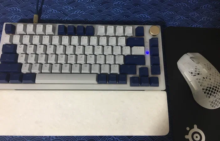 Clavier Feker IK75 Pro à keycaps bleu et blanc, souris Steelseries Aerox 3 Wireless blanche sur tapis noir.