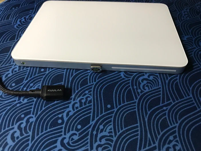 Face arrière d'un ordinateur blanc avec un connecteur de câble magnétique noir marqué KUULAA sur fond bleu.